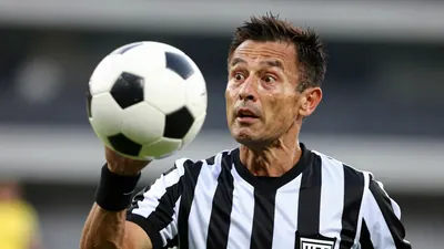 Photorealistic image of a referee in a black and white striped shirt, mid-30s, with short dark hair, reacting to being...