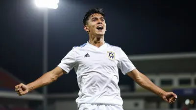 A tight action shot of a young Mexican footballer in a white jersey, mid-celebration after scoring a header in stoppage time